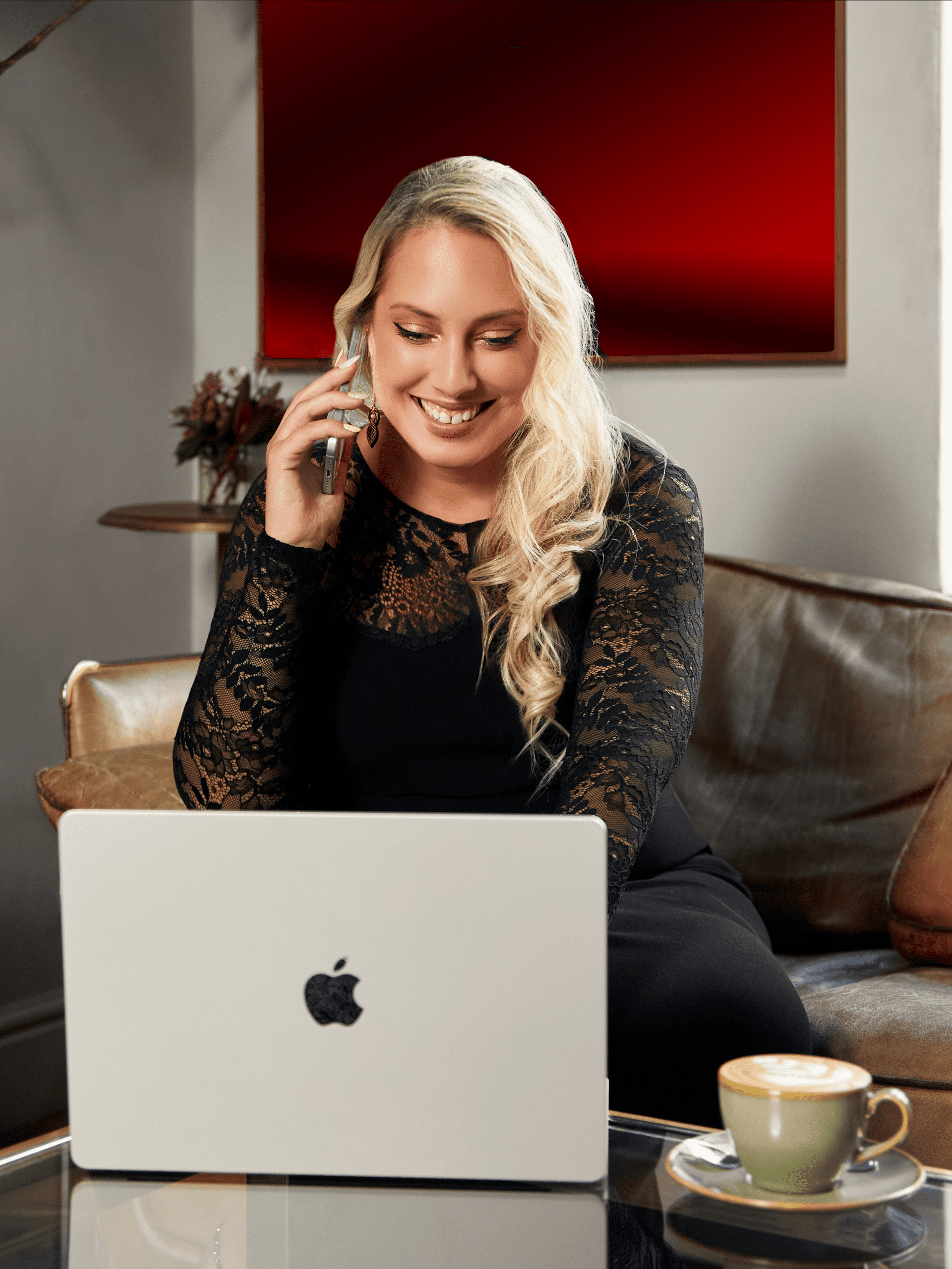 Smiling woman on phone with laptop and notebook in cozy workspace.