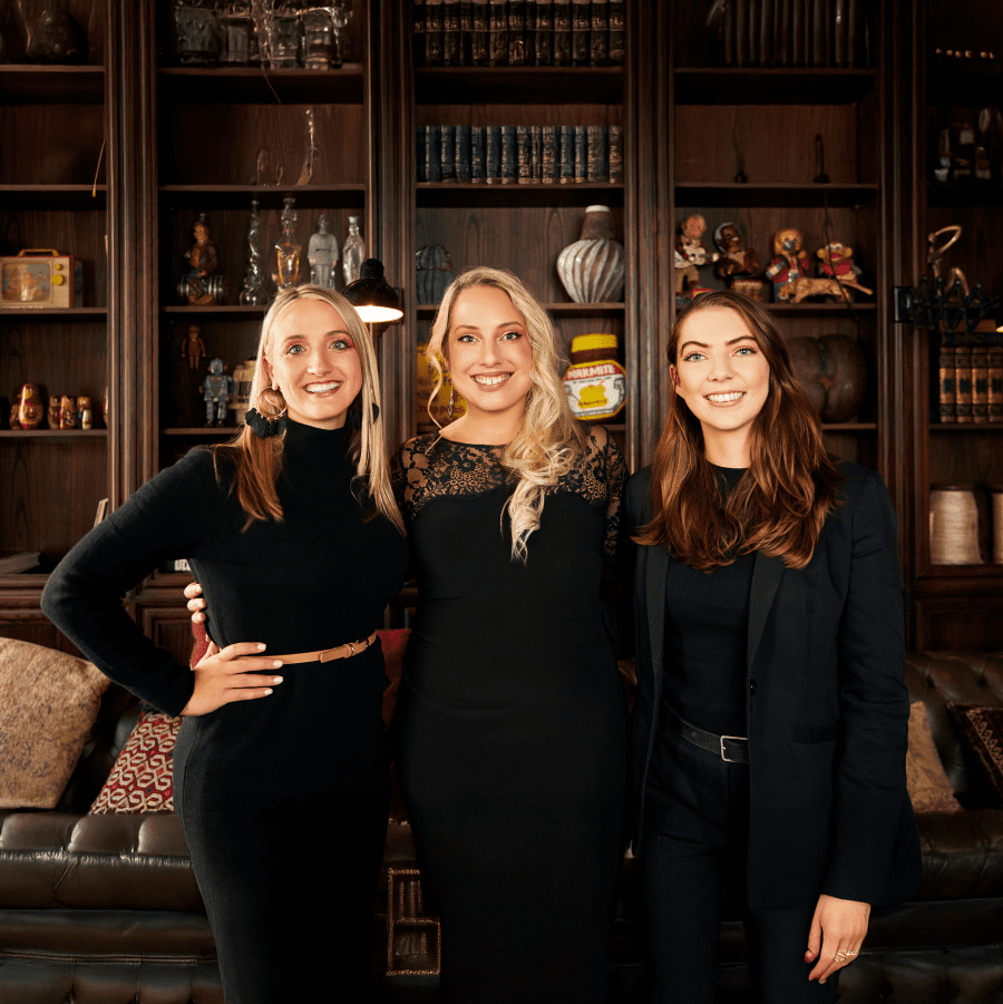 Group of three women in black outfits posing together indoors.