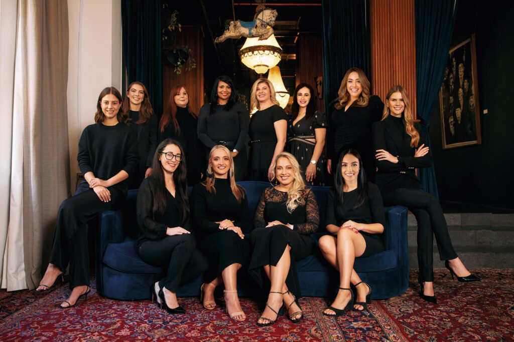 Large group of women dressed in black posing together in elegant setting.