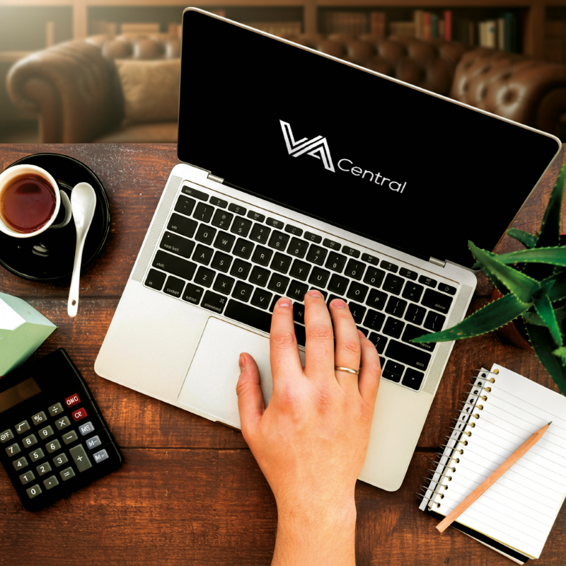 Person typing on laptop with phone beside and scenic image on screen.